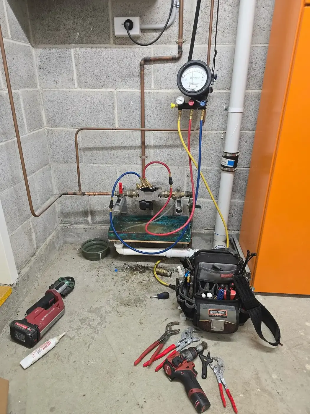 Backflow testing gauge and hoses connected to a backflow valve against a block wall
