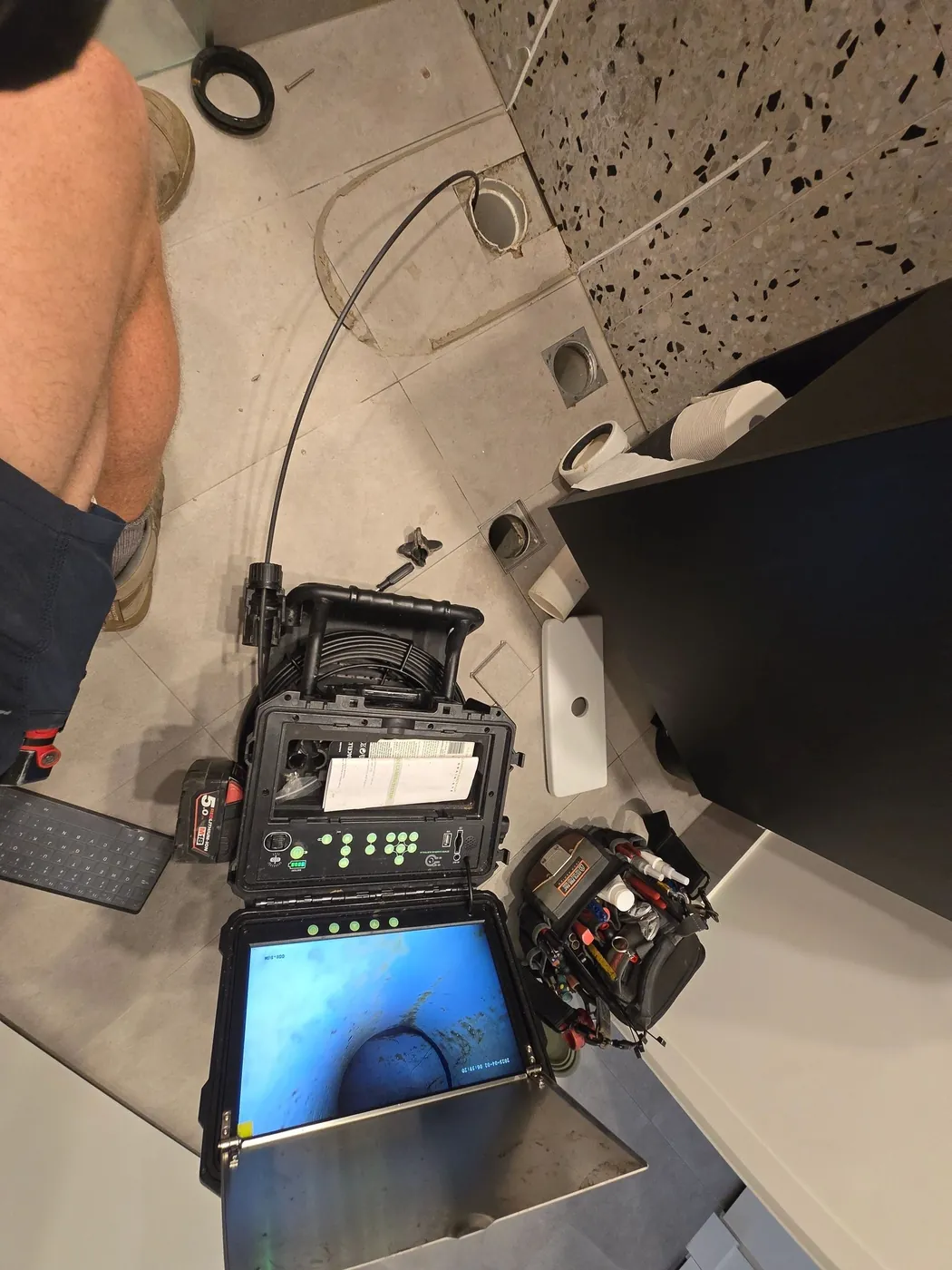 Drain camera screen and cable set up beside an open drain inside a building
