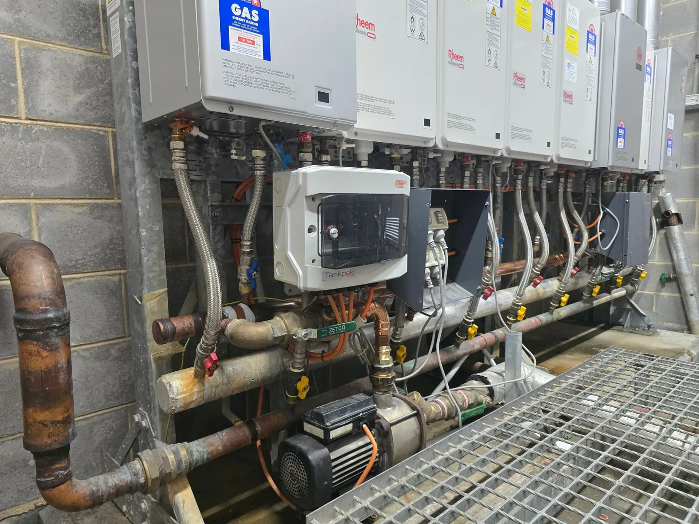 Row of gas hot water units with pumps and pipework in a plant area