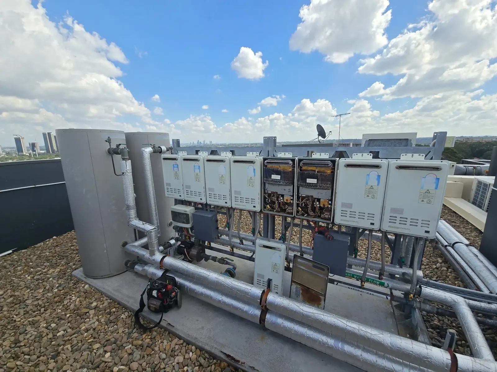 Bank of gas hot water units and storage tanks on a rooftop, with insulated pipework